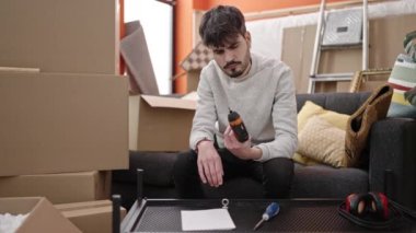 Genç İspanyol adam yeni evinde matkapla yeni bir masa kuruyor.