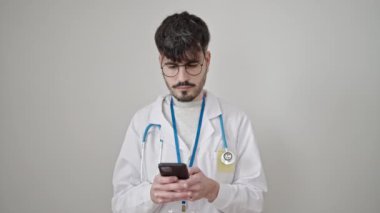 Genç İspanyol doktor, izole edilmiş beyaz arka plan üzerinde akıllı telefon kullanarak gülümsüyor.
