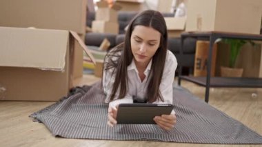 Genç ve güzel İspanyol kadın dokunmatik ped kullanıyor. Yeni evinde yerde yatıyor.