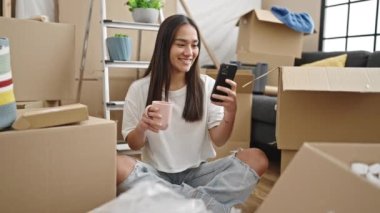 Genç, güzel, İspanyol bir kadın akıllı telefon kullanıyor. Yeni evinde kahve içiyor.