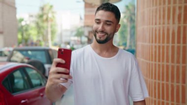 Genç Arap adam kendinden emin gülümsüyor. Sokakta akıllı telefonun yanında selfie çekiyor.