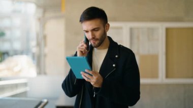 Genç İspanyol adam, elinde touchpad ile akıllı telefondan konuşuyor.