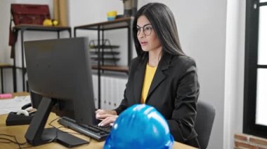 Kollarını kavuşturup ofiste bilgisayar arayan genç, güzel İspanyol bir mimar.