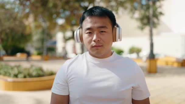 若いです中国人男性リッスンで音楽とともにリラックスした表現で公園 — ストック動画