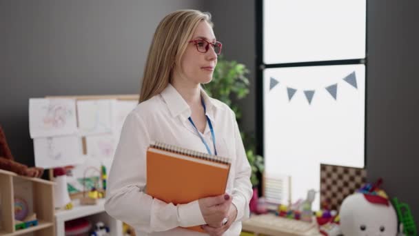 Young Blonde Woman Preschool Teacher Smiling Confident Holding Books Kindergarten — Vídeos de Stock