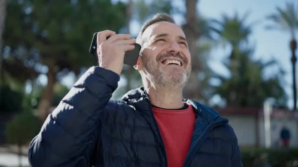 中年男性笑顔自信に満ちたリスニング音声メッセージによってスマートフォンによって公園 — ストック動画