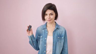 Genç beyaz kadın gülümsüyor. Kendine güveni tam. Yeni arabanın anahtarını pembe arka planda tutuyor.