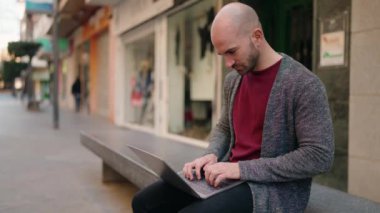 Sokakta dizüstü bilgisayar kullanan kel bir adam.
