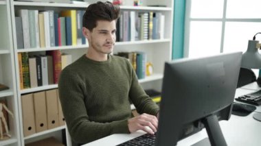 Young hispanic man student using computer studying at library university