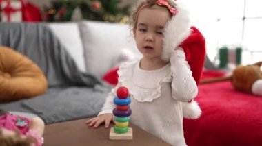 Beyaz kız oyuncakla oynuyor. Evde Noel ağacının yanında duruyor.