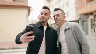 Genç çift sokakta akıllı telefonun yanında kendinden emin bir şekilde selfie çekiyor.