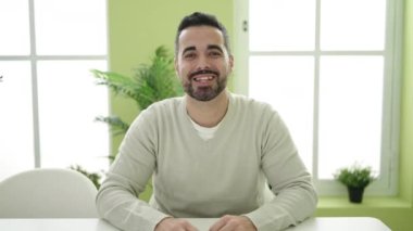 Young hispanic man sitting on table speaking at home