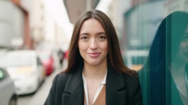 Genç İspanyol kadın gülümsüyor. Kollarını kavuşturup caddede duruyor.