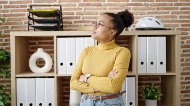 Ofiste kollarını kavuşturmuş gözlüklü gülümseyen genç Afrikalı Amerikalı kadın.