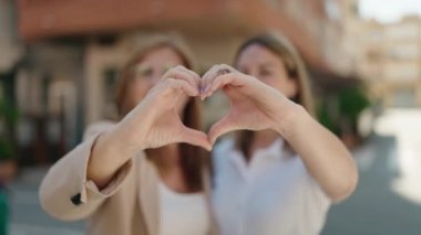 Mother and daughter smiling confident doing heart symbol with hands at street