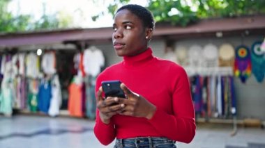 Sokak pazarında gülümseyen akıllı telefon kullanan Afrikalı Amerikalı kadın.