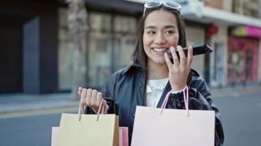 Güzel İspanyol bir kadın elinde alışveriş torbalarıyla akıllı telefonuyla sesli mesaj yolluyor.