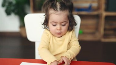 Anaokulunda masaya oturmuş kağıda resim çizen sevimli İspanyol kız öğrenci.