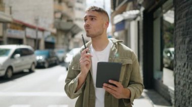 Young hispanic man smiling confident drawing on touchpad at street