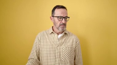 Orta yaşlı bir adam, öfkeli bir ifadeyle, izole edilmiş sarı arka planı parmağıyla işaret ediyor.