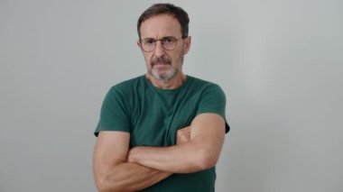 Orta yaşlı bir adam, ciddi bir ifadeyle ve kollarını kavuşturarak izole edilmiş beyaz arka planda duruyor.