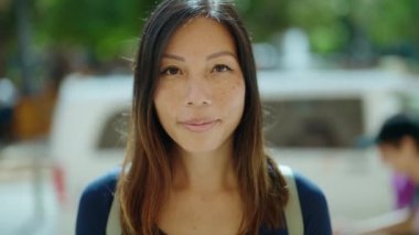 Genç Asyalı kadın parkta kendinden emin bir şekilde gülümsüyor.