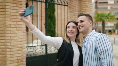 Birbirlerine sarılan erkek ve kadın çift sokakta akıllı telefonlardan selfie çekiyorlar.