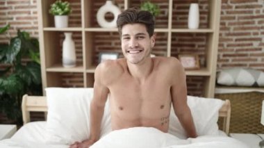 Young hispanic man smiling confident sitting on bed at bedroom