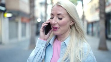 Genç sarışın kadın gülümsüyor. Kendine güveni tam. Akıllı telefondan konuşuyor.