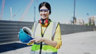 Young beautiful hispanic woman architect smiling confident wearing hardhat at street