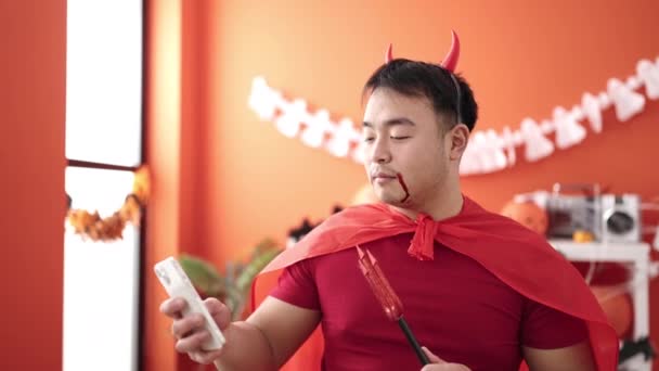 若いです中国人男身に着けている悪魔衣装作る自画撮りによってスマートフォン ホーム — ストック動画