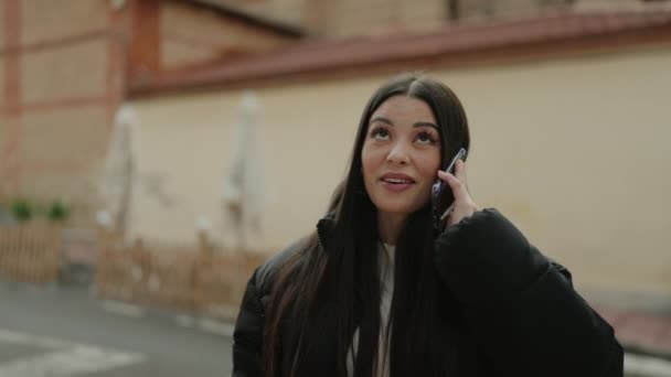 若いヒスパニック系の女性が路上でスマートフォンで自信を持って話して笑顔 — ストック動画