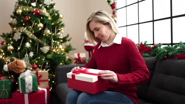 Young Blonde Woman Unpacking Gift Sitting Sofa Christmas Tree Home — Stock Video