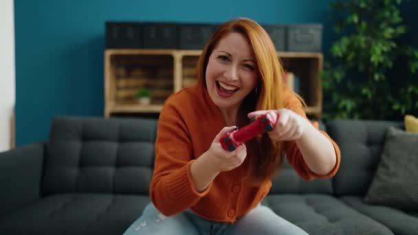 年轻的红头发女人坐在家里沙发上玩电子游戏 — 图库视频影像
