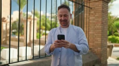 Sokakta akıllı telefon kullanan, kendinden emin gülümseyen beyaz bir genç.