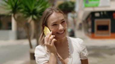 Beyaz bir kadın gülümsüyor ve caddede akıllı telefondan konuşuyor.
