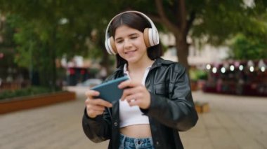 Parkta video oyunu oynarken gülümseyen genç İspanyol kadın.