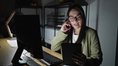 Genç, güzel İspanyol iş kadını. Ofiste akıllı telefondan konuşan tablet kullanıyor.