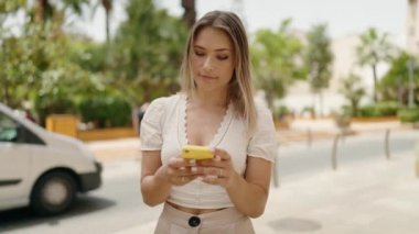 Beyaz kadın gülümsüyor. Sokakta akıllı telefonun yanında özçekim yapıyor.