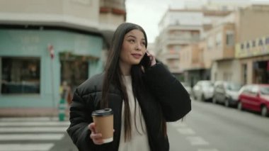 Genç İspanyol kadın akıllı telefonda konuşuyor. Sokakta kahve içiyor.