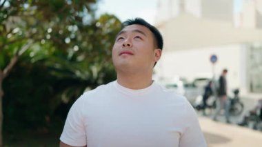 Young chinese man smiling confident looking to the sky at park
