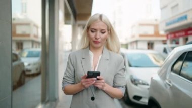 Genç sarışın kadın yönetici caddede akıllı telefon kullanıyor.
