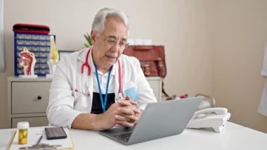 Gri saçlı bir doktorla orta yaşlı bir adam klinikte internetten randevu alıyor.