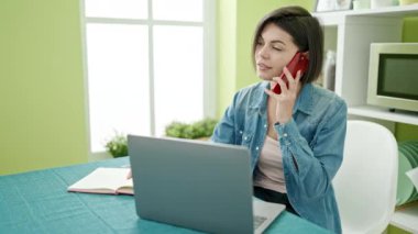Beyaz bir kadın akıllı telefonuyla evde dizüstü bilgisayar kullanıyor.