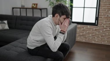 Young hispanic man stressed sitting on sofa at home
