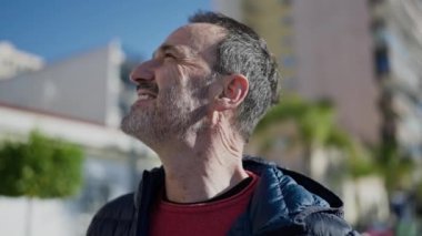 Orta yaşlı bir adam sokakta kendine güvenerek gülümsüyor.