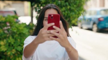 Young beautiful hispanic woman smiling confident make photo by smartphone at street