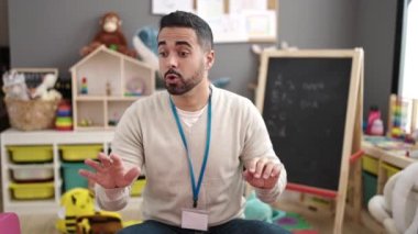 Young hispanic man preschool teacher asking for silence at kindergarten