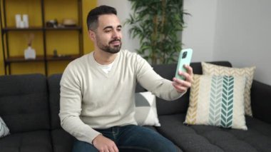 Evdeki kanepede oturan Latin asıllı genç bir adam.