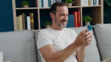 Middle age man using smartphone sitting on sofa at home
